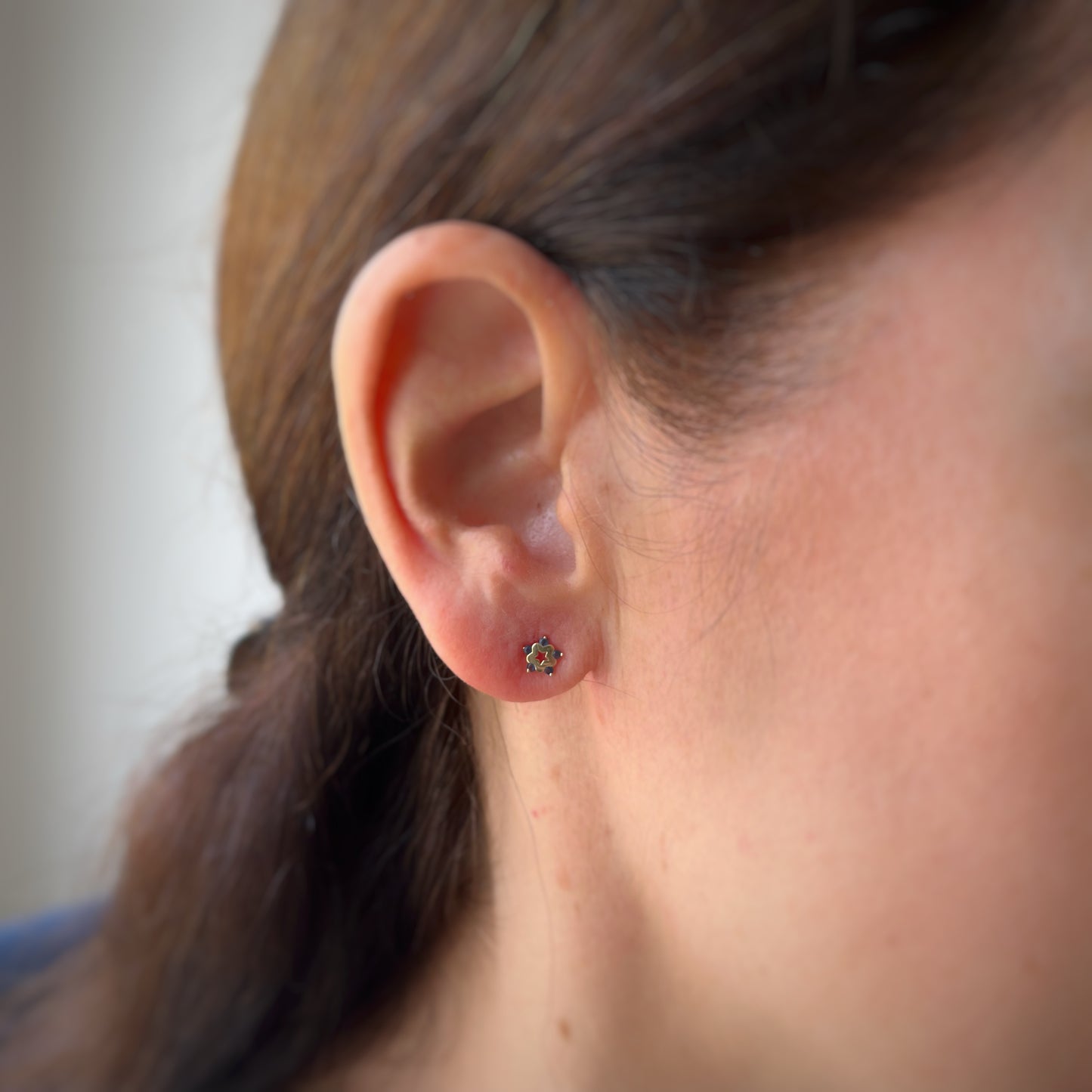 Arete en oro amarillo de 14K con estrella tipo flor con circonita azul en los extremos y estrella calada en el centro con tope rosca