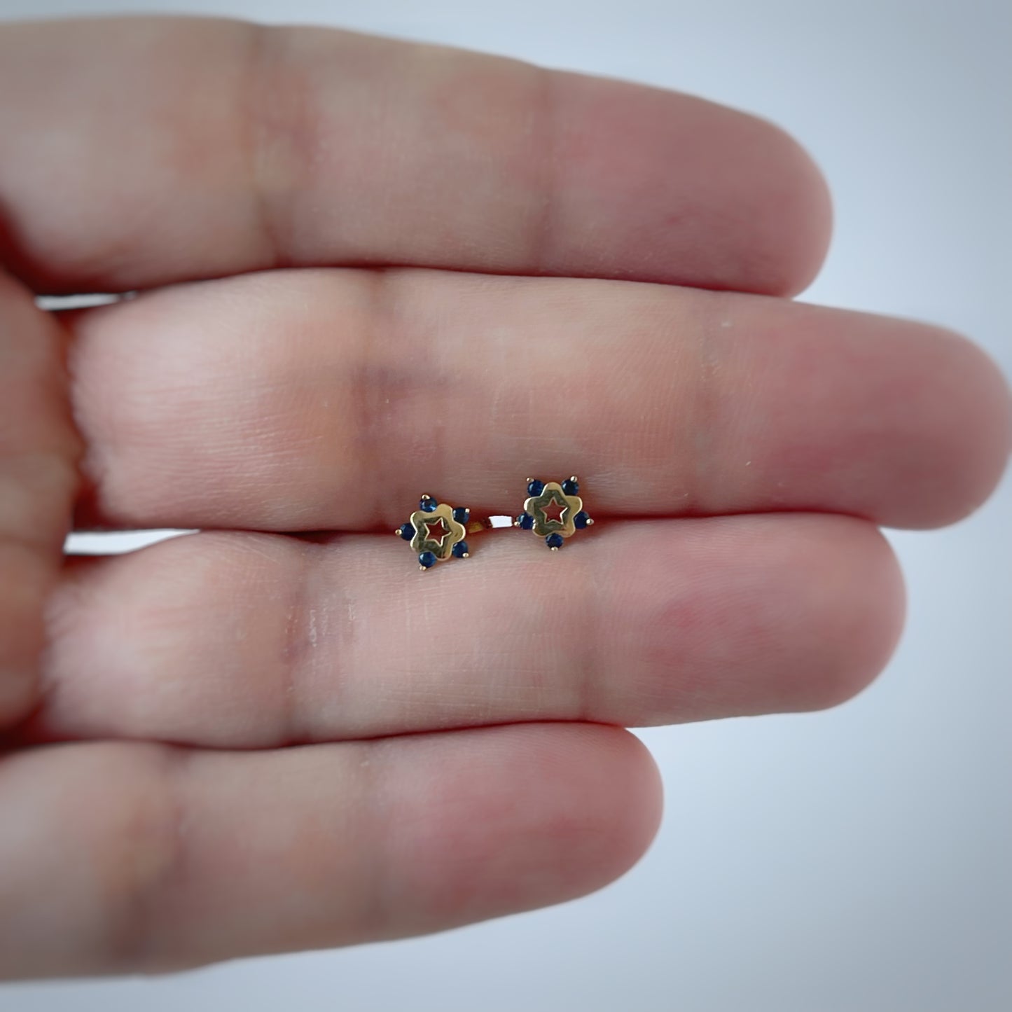 Aretes en oro amarillo de 14K con estrella tipo flor con circonita azul en los extremos y estrella calada en el centro con tope rosca