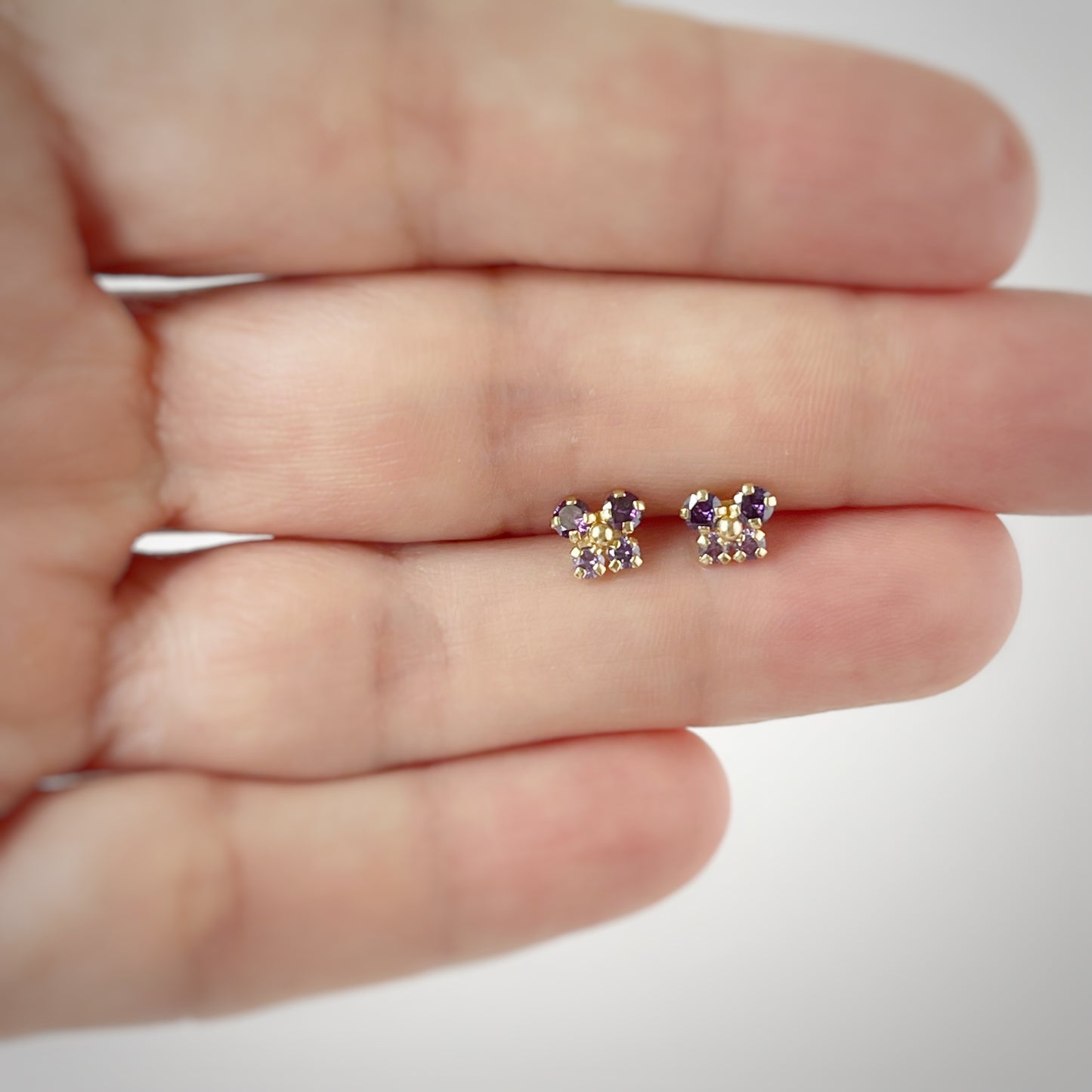 Aretes en oro amarillo 14K con mariposa con circonita morada con dos tonos y bolita de oro en el centro con tope rosca