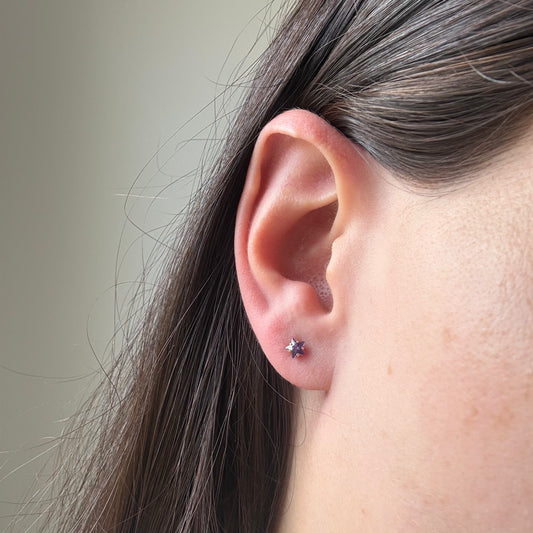 Aretes mini estrella con circón lila en oro amarillo 14K con tope rosca