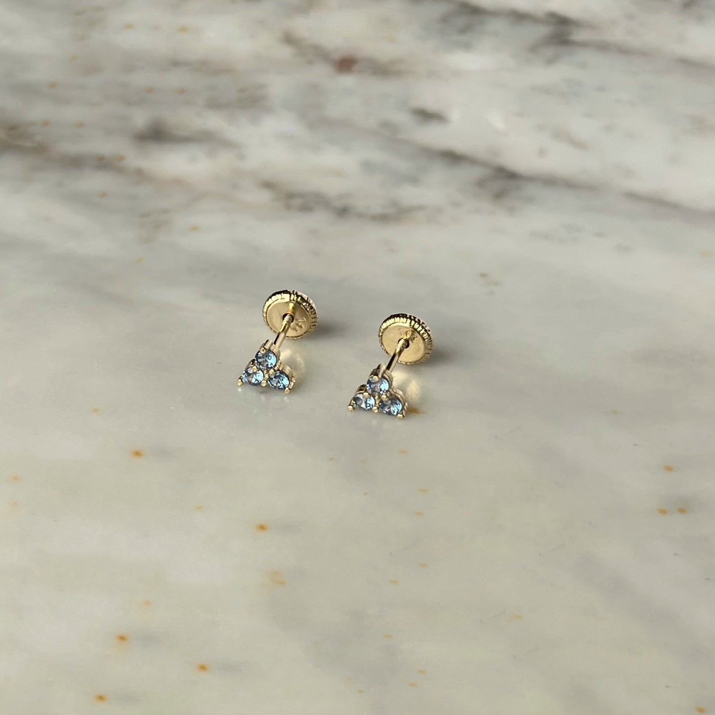Aretes tres circonitas color celeste de 3mm en forma de triángulo en oro amarillo de 14k con tope ortopédico