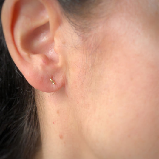 Aretes single en oro amarillo 14k de 3 bolitas y rosca interna para piercing