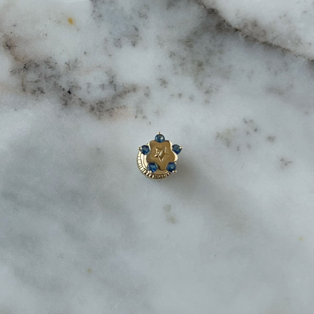 Arete en oro amarillo de 14K con estrella tipo flor con circonita azul en los extremos y estrella calada en el centro con tope rosca