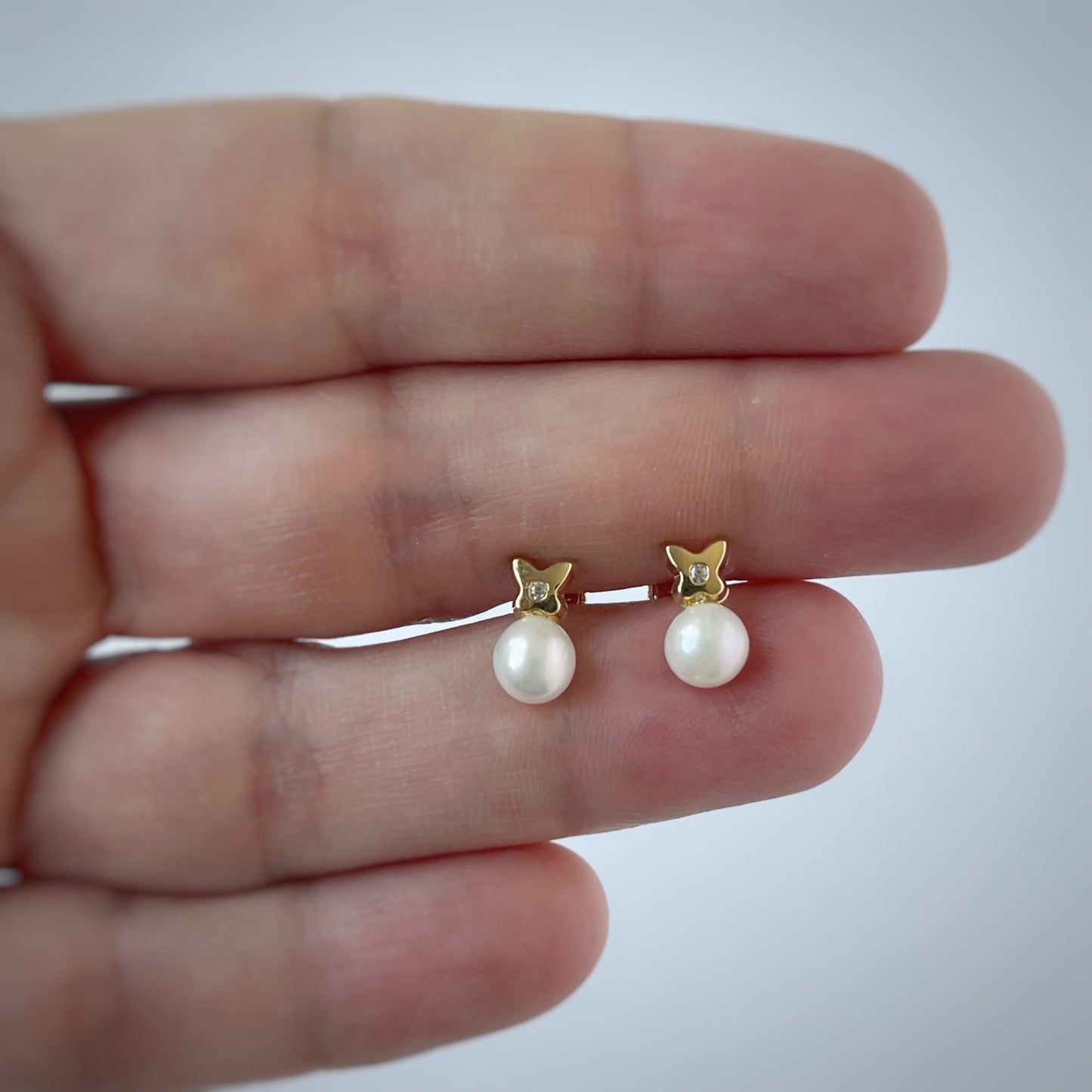 Aretes en oro amarillo de 14K con perla abajo y flor de cuatro pétalos arriba con circonita blanca en el centro y tope rosca