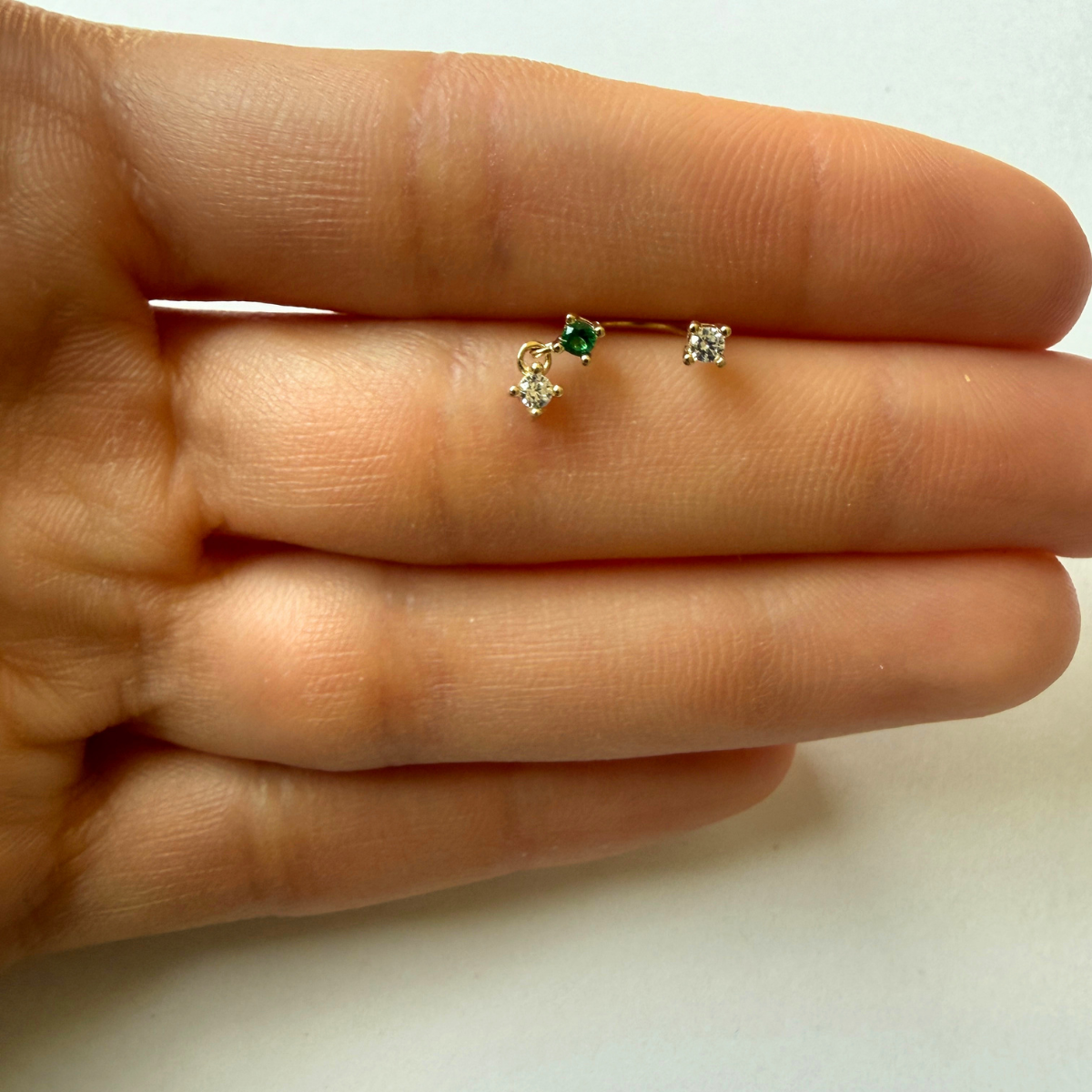 Arete piercing curva en oro amarillo 14k con circonitas blancas y verde