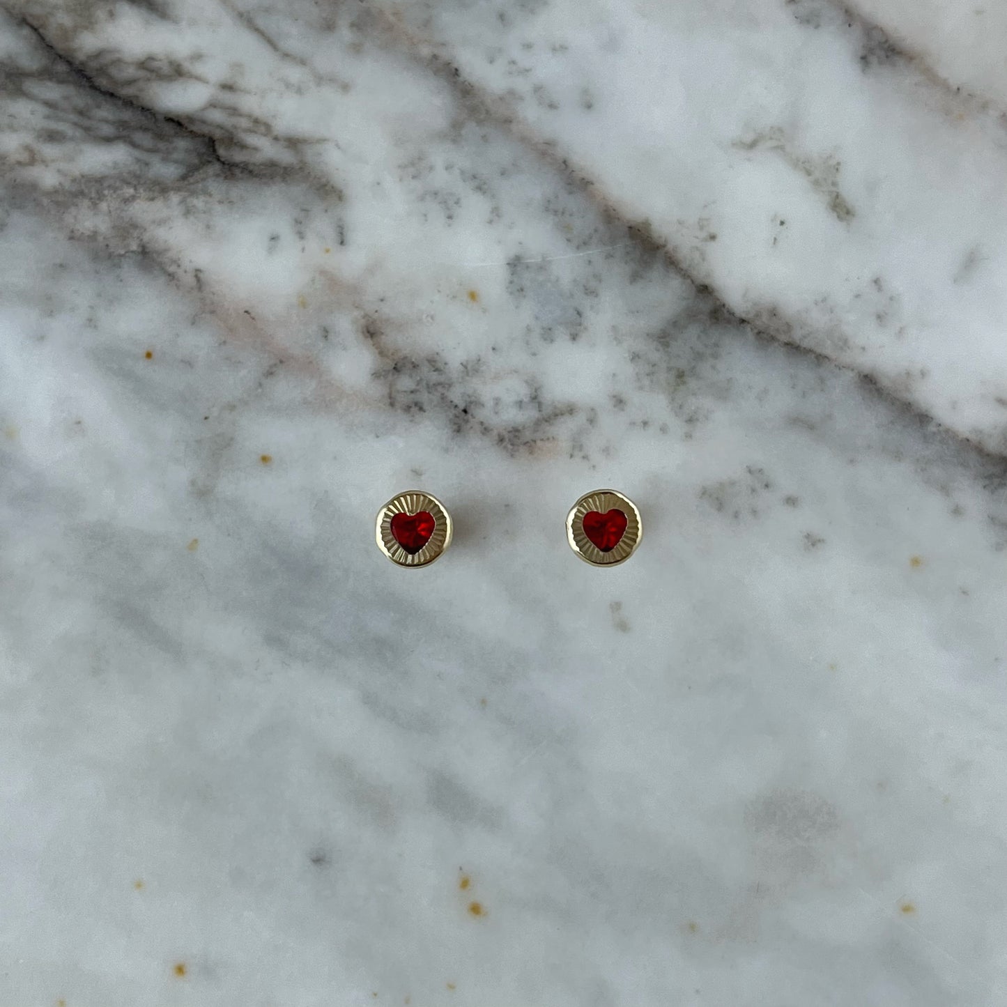 Aretes en oro amarillo 14K con círculo de rayitas y centro con corazón de circonita roja con tope rosca