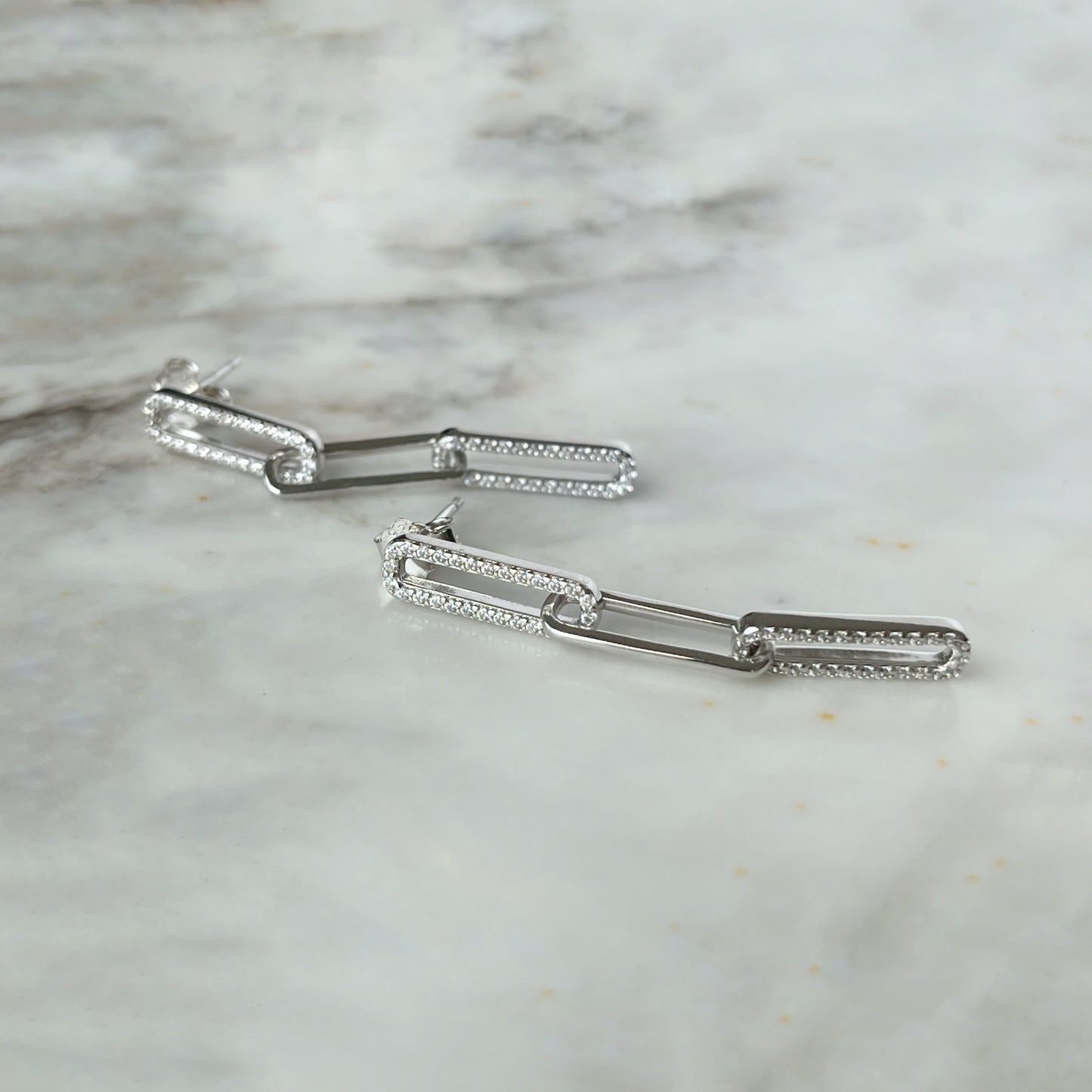 Arete largo paper clip de plata con baño platino y circonitas blancas