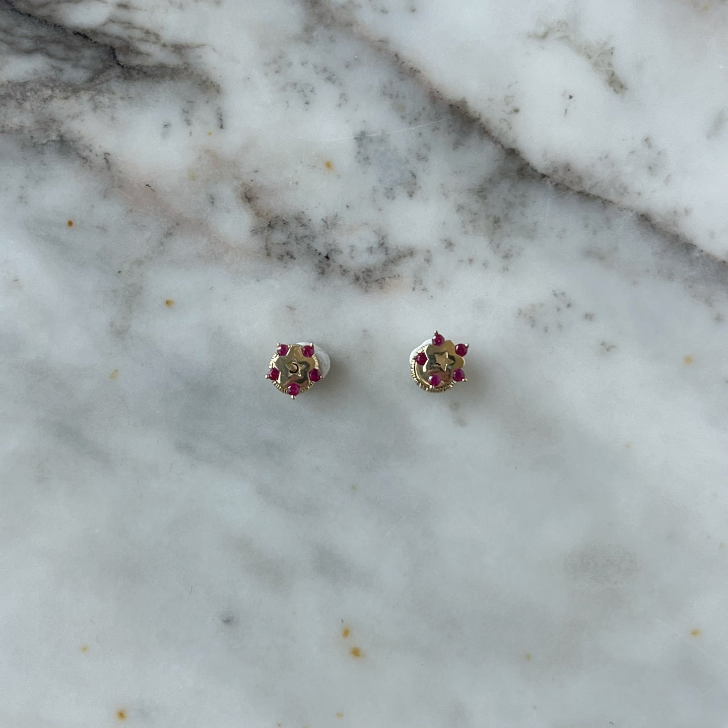 Aretes en oro amarillo de 14K con estrella tipo flor con circonita fucsia en los extremos y estrella calada en el centro con tope rosca