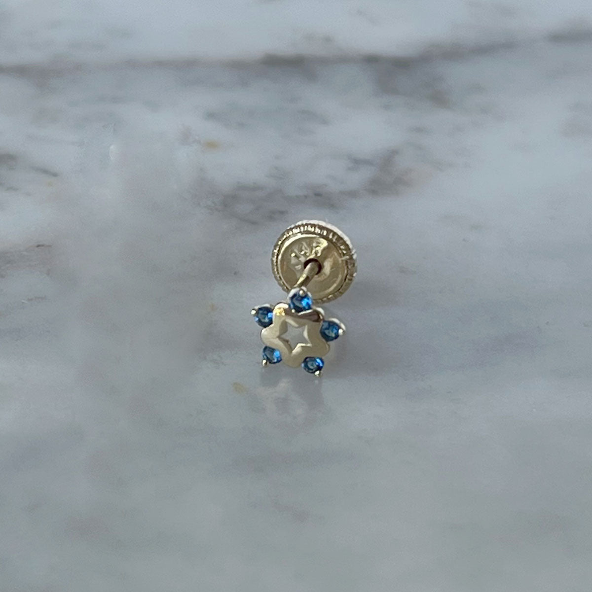 Arete en oro amarillo de 14K con estrella tipo flor con circonita azul en los extremos y estrella calada en el centro con tope rosca