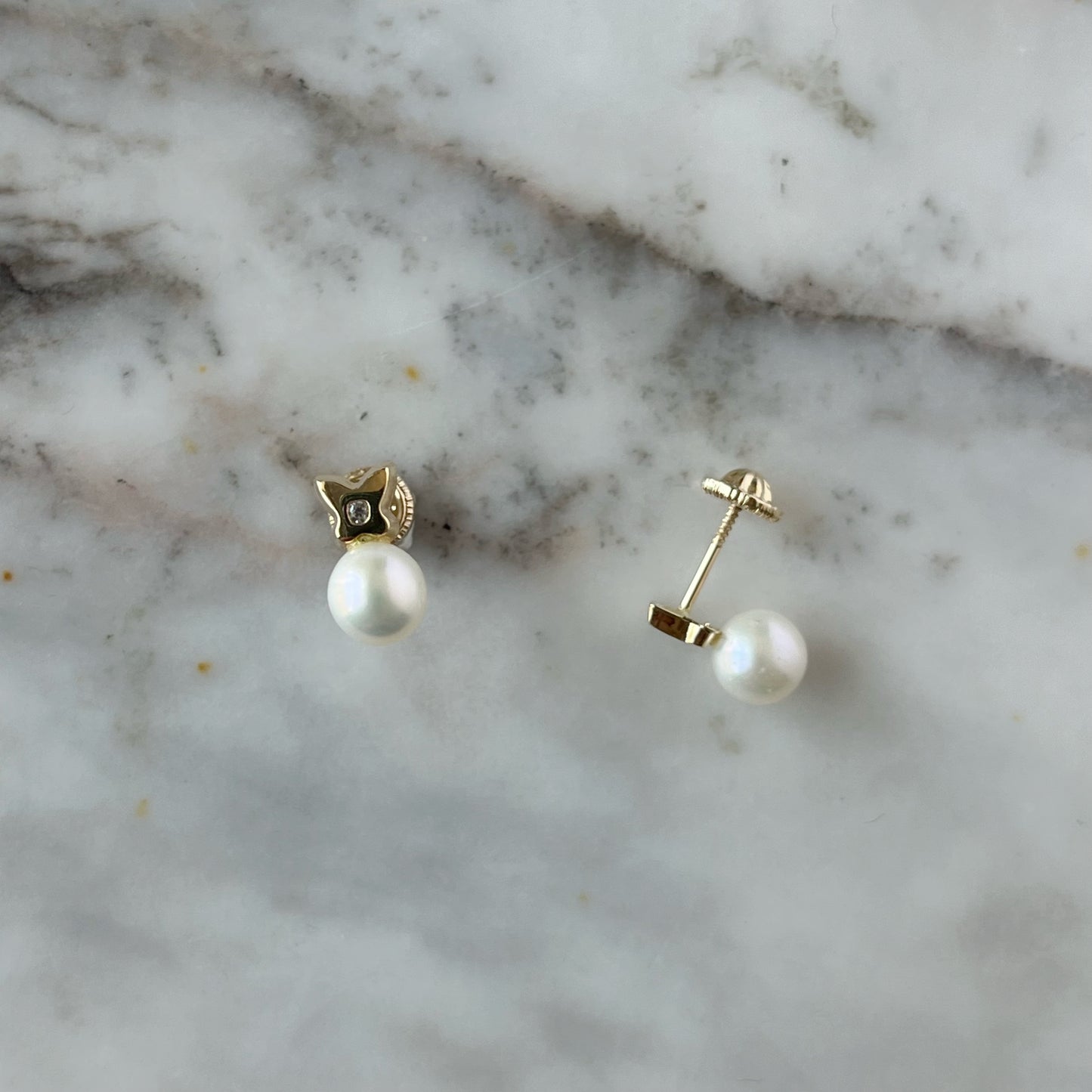 Aretes en oro amarillo de 14K con perla abajo y flor de cuatro pétalos arriba con circonita blanca en el centro y tope rosca