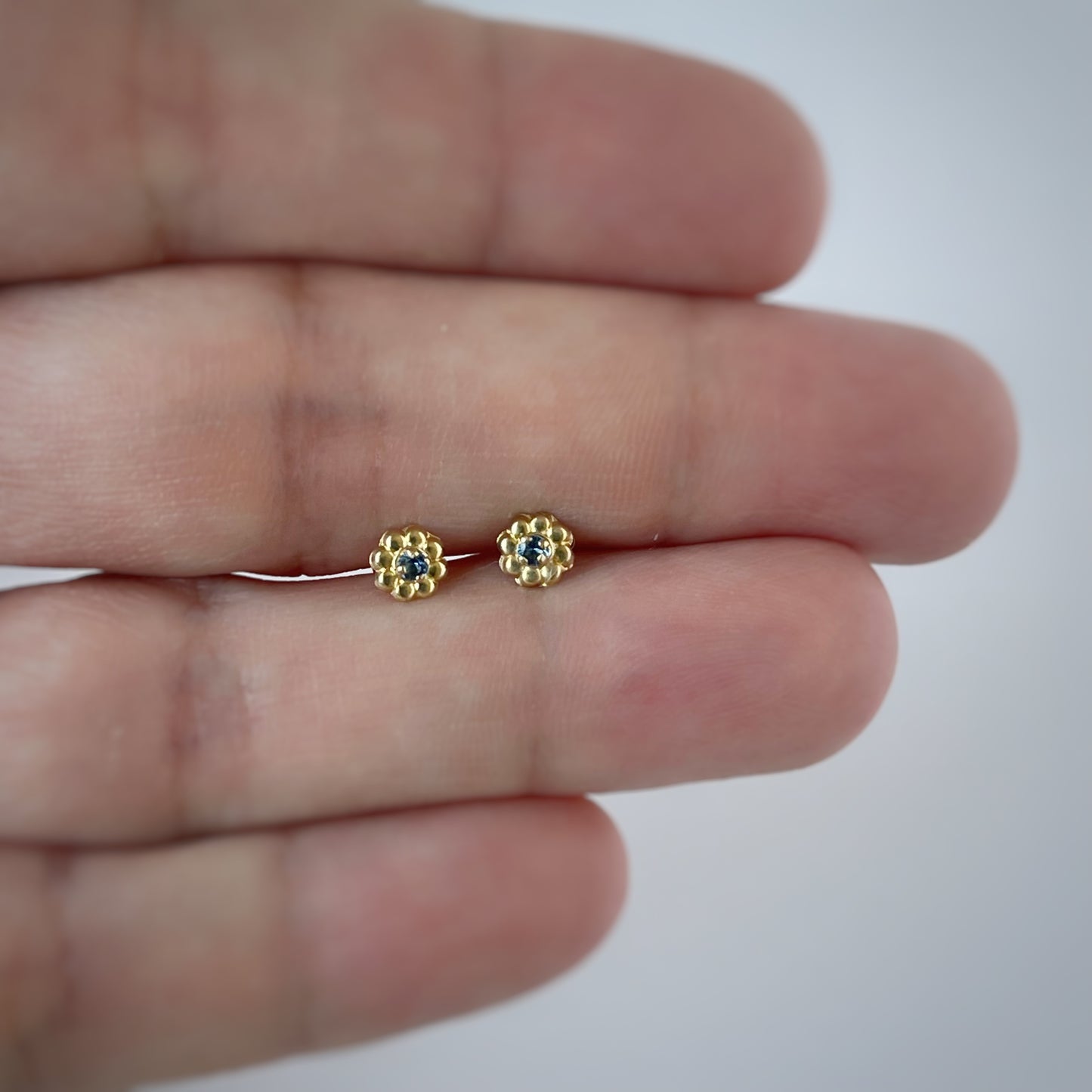 Aretes en oro amarillo 14K con flor de pétalos de oro y circonita azul en el centro con tope a rosca