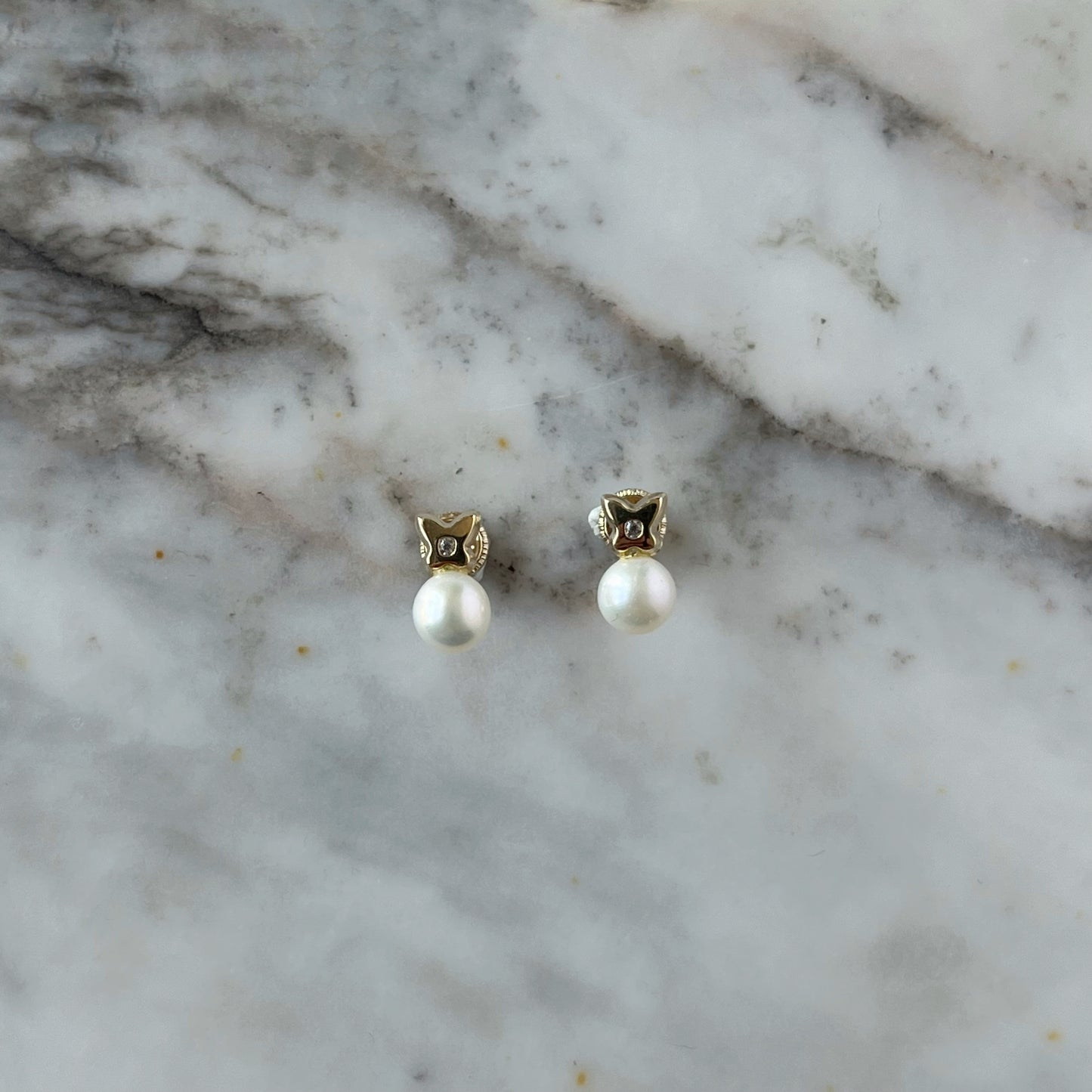 Aretes en oro amarillo de 14K con perla abajo y flor de cuatro pétalos arriba con circonita blanca en el centro y tope rosca