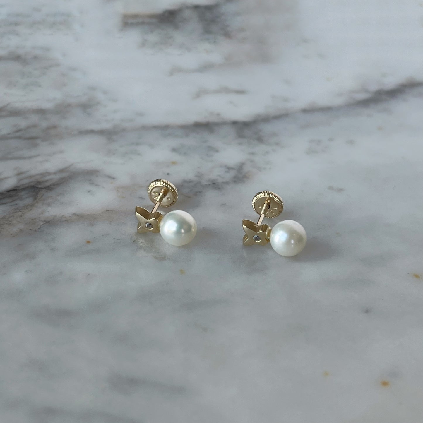 Aretes en oro amarillo de 14K con perla abajo y flor de cuatro pétalos arriba con circonita blanca en el centro y tope rosca