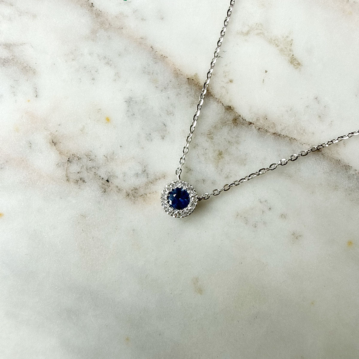 Collar en oro blanco 14k con zafiro redondo 0.13ct y halo de diamantes 0.04ctw