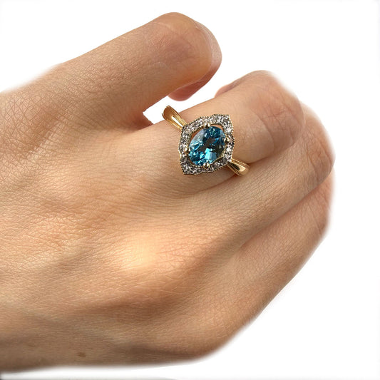Anillo en oro amarillo 14K con topacio azul ovalado y borde de diamantes 0.10ctw